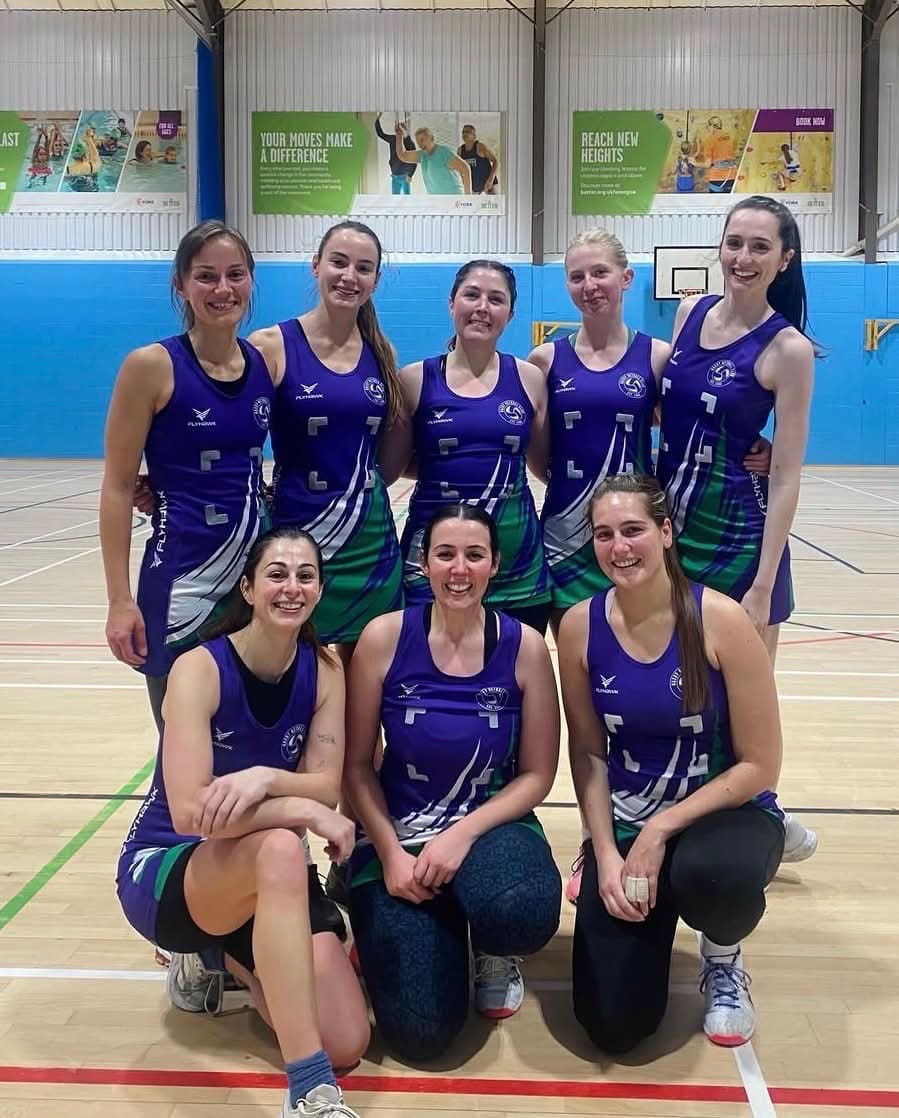 Eight Haxby Netball players in purple and green kit, gathered together on court after a league fixture.