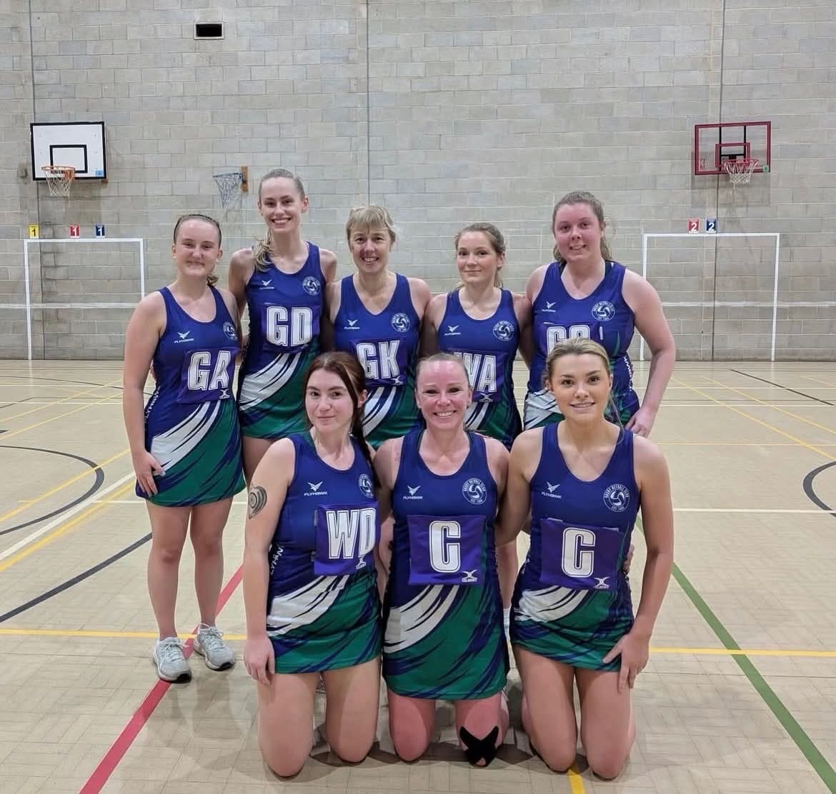 Haxby Netball's senior squad in blue and green kit, wearing position bibs, posed together on court after a match.