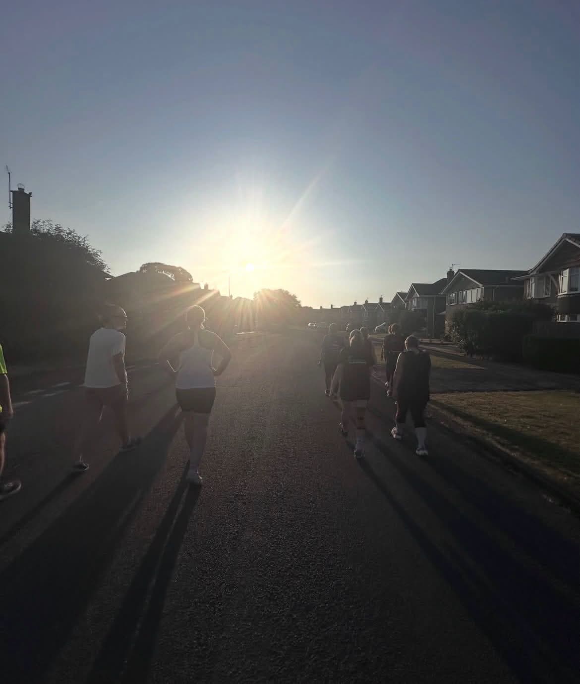 Haxby Runners setting out along a village road at sunrise, silhouetted against a low sun with long shadows behind them.